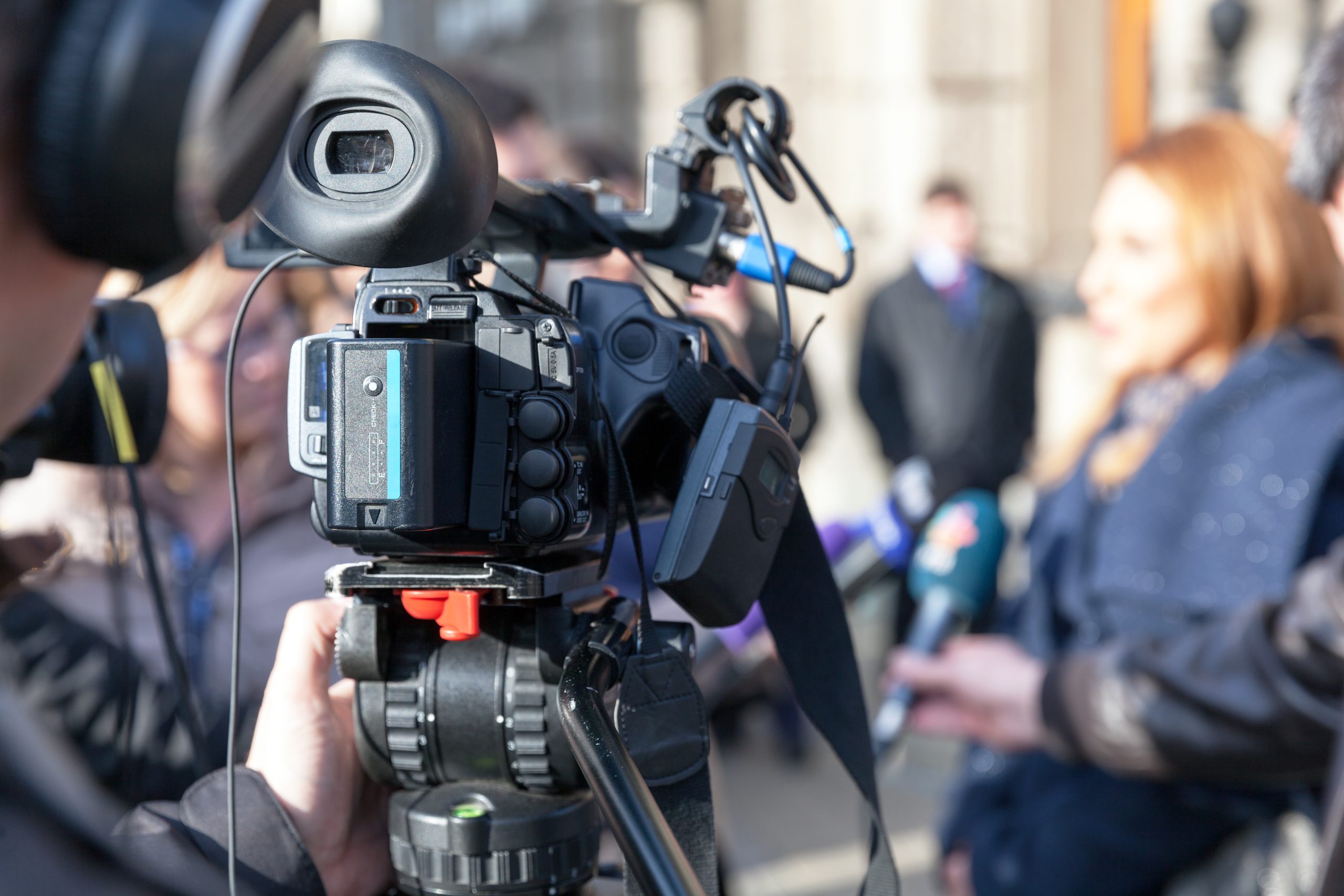 Image of video camera with person faded in background.